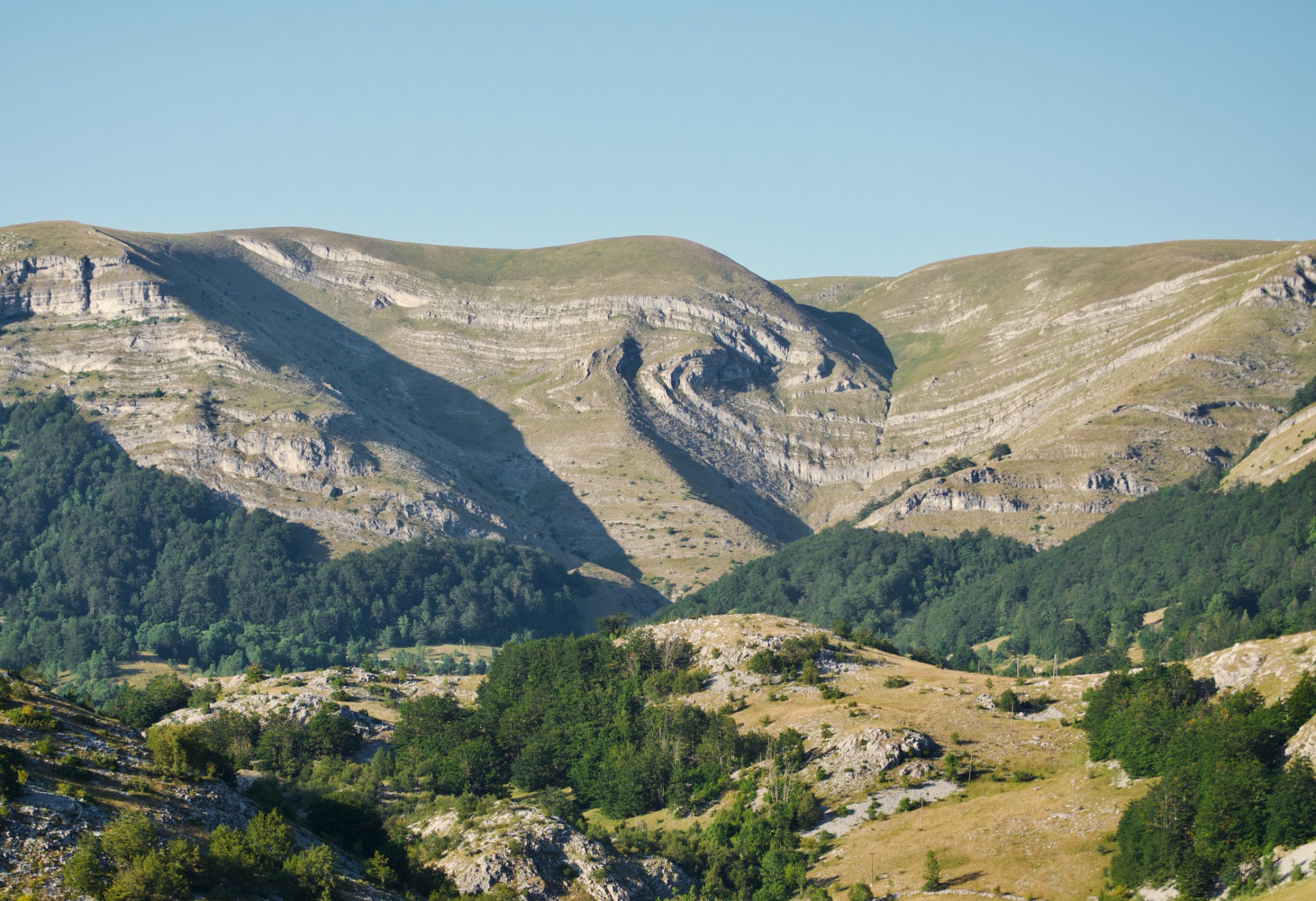 A photo of massive, rolling mountains featuring a distinctive, swirling rock pattern in the center where the stratified layers twist sharply.
